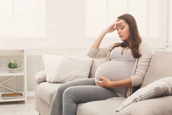 Jeune femme enceinte avec mal de tête assis sur le canapé — Photo