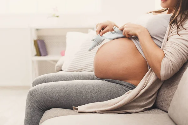 Donna incinta che tiene piccole scarpe vicino alla pancia — Foto Stock