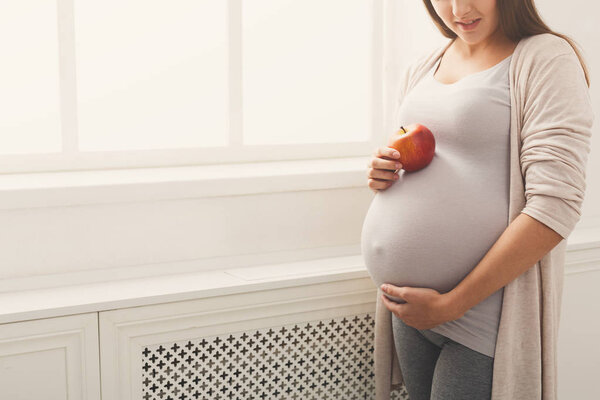 Pregnant woman eating apple at home copy space