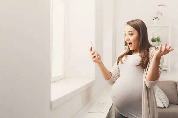 Здивована вагітна жінка за допомогою смартфона — стокове фото