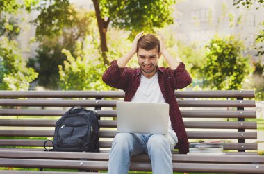 Bir dizüstü bilgisayar açık havada kullanan umutsuz genç adam