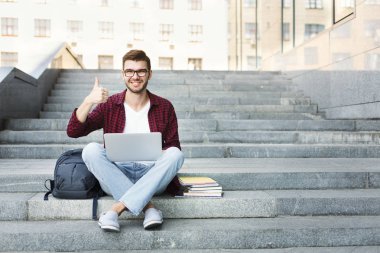 Açık havada yukarı gösterilen merdivenlerde oturan öğrenci