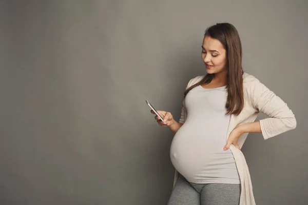 Senyum wanita hamil menggunakan smartphone — Stok Foto