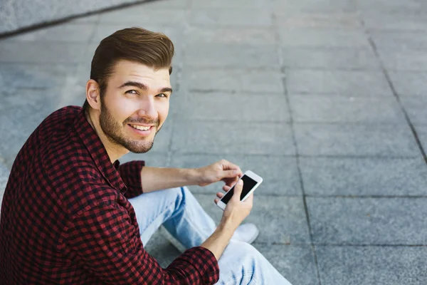 Sorrindo jovem usando seu telefone ao ar livre — Fotografia de Stock