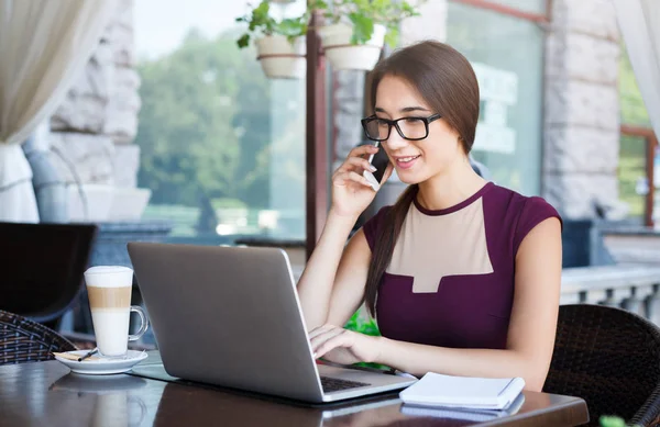 Jonge zakenvrouw die op laptop werkt en praten over de telefoon — Stockfoto