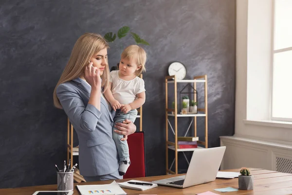 Молода мати тримає дитину, розмовляючи по телефону — стокове фото