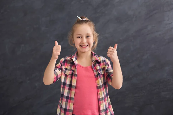 Casual little girl showing thumbs up at gray background — Stock Photo, Image