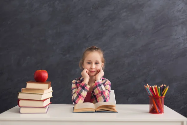 Nettes intelligentes Mädchen lächelt, während es mit Büchern am Tisch sitzt — Stockfoto