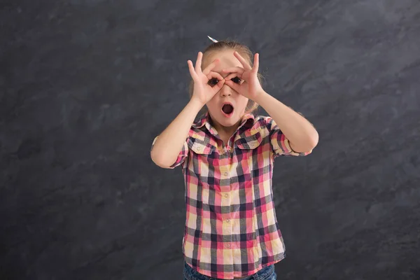 Lässiges weibliches Kind hält Finger wie Brille in der Nähe der Augen — Stockfoto