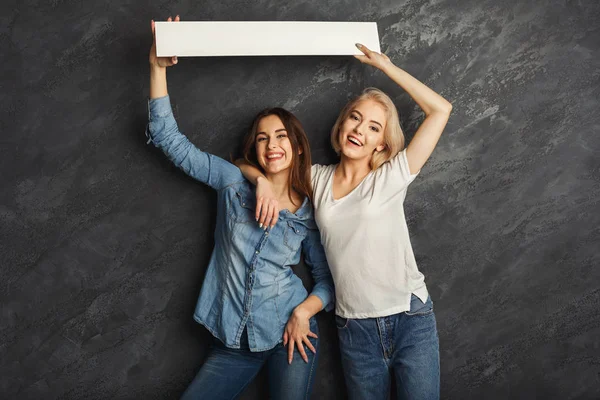 Filles heureuses avec bannière blanche vierge au fond sombre studio — Photo