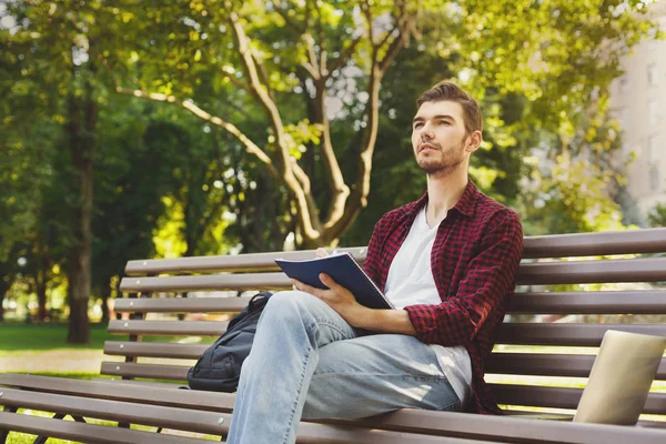 Young man thinking with a copy-book outdoors — Stock Photo, Image