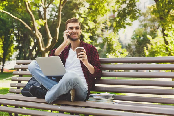 Hombre con portátil, hablando en el teléfono inteligente al aire libre — Foto de Stock