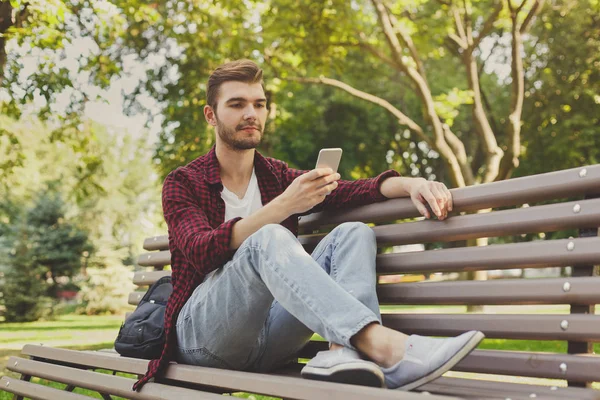 Bonito homem sentado e usando smartphone ao ar livre — Fotografia de Stock