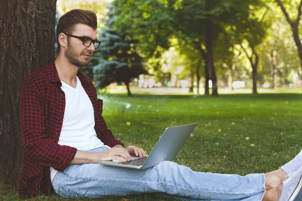 Hombre sentado en la hierba con el ordenador portátil al aire libre — Foto de Stock
