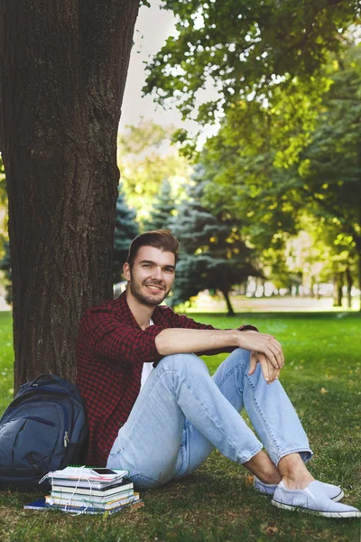 Jovem homem bonito sentado na grama ao ar livre — Fotografia de Stock