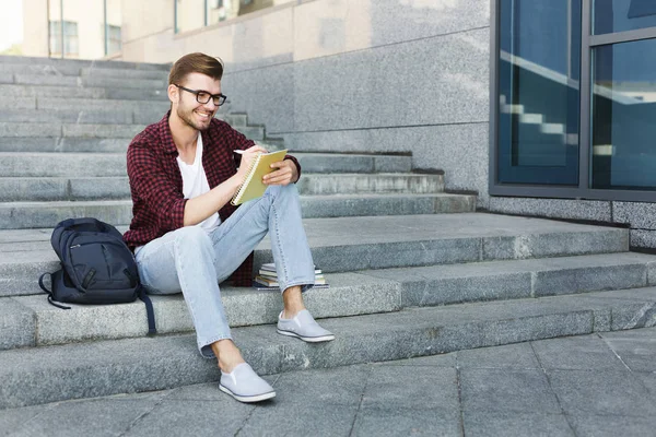 Estudiante atractivo haciendo notas sentado en las escaleras al aire libre — Foto de Stock