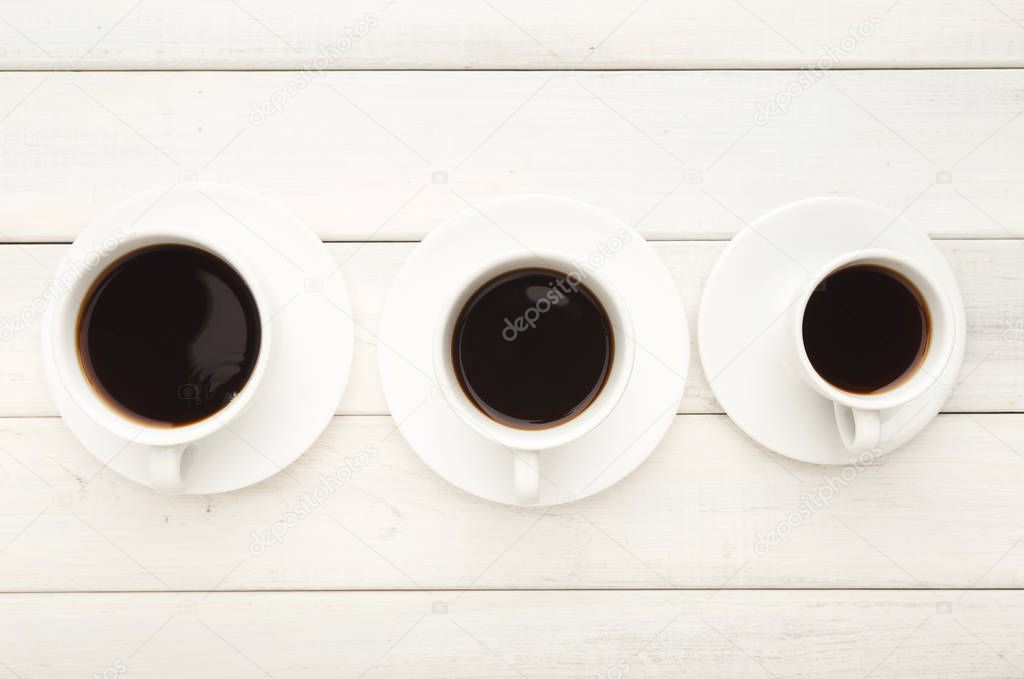 Various cups with black coffee on white wooden table