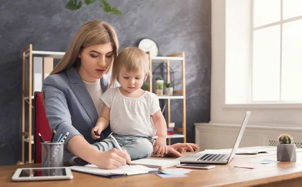 Joven madre sosteniendo bebé mientras escribe notas — Foto de Stock