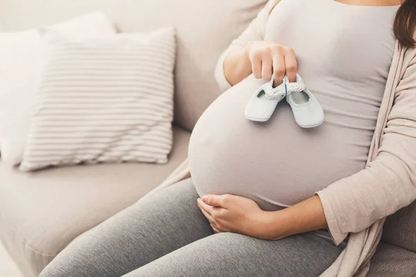 Pregnant woman holding tiny shoes near belly — Stock Photo, Image