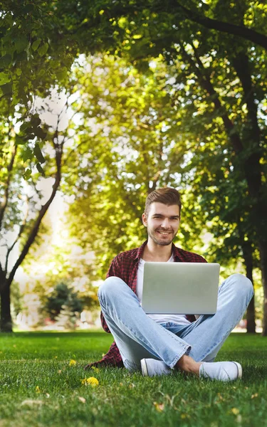 Feliz hombre está sentado en el parque y el uso de ordenador portátil — Foto de Stock