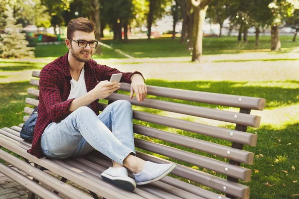 Hombre guapo sentado y usando el teléfono inteligente al aire libre — Foto de Stock