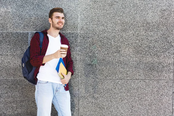 Hermoso estudiante sosteniendo taza de café sobre fondo gris al aire libre —  Fotos de Stock