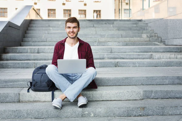 Estudiante sentado en las escaleras y trabajando con el ordenador portátil al aire libre — Foto de Stock