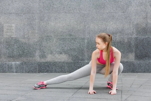 Beautiful young woman stretching against grey wall — Stock Photo, Image