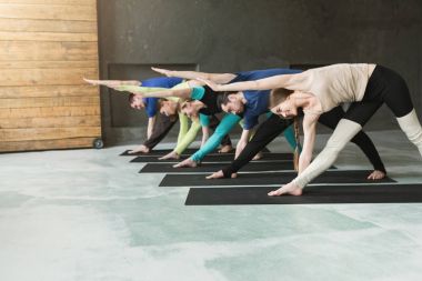 Genç kadın ve erkekler yoga sınıfındaki germe egzersizleri yapıyor