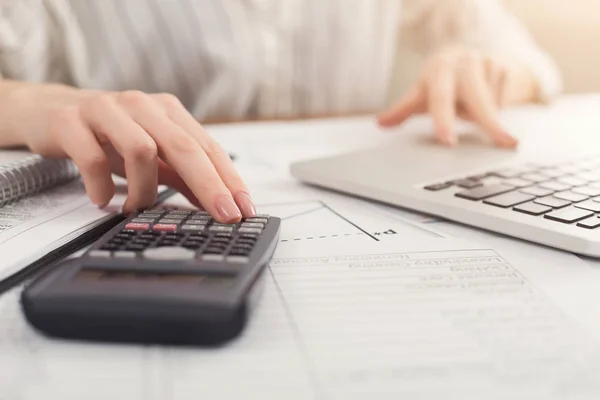 Primer plano de las manos de la mujer contando con la calculadora y escribiendo en el ordenador portátil — Foto de Stock