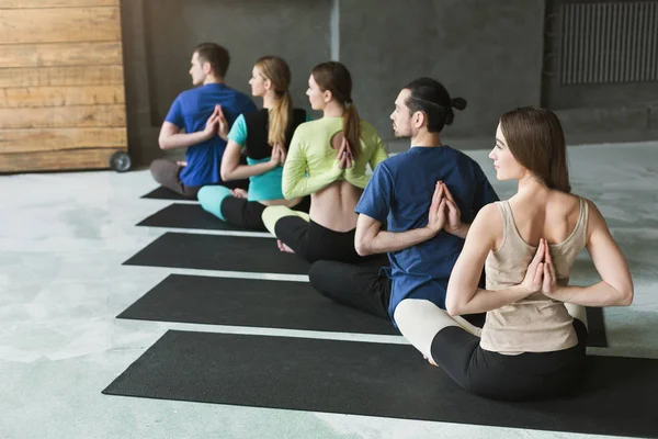 Mujeres jóvenes y hombres en clase de yoga, relajar la meditación pose — Foto de Stock