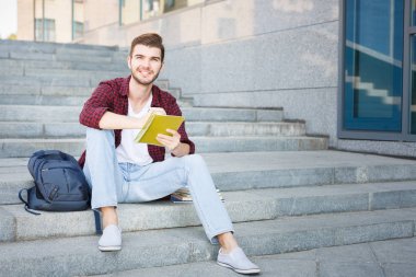 Merdivenlerde oturan ve açık havada notlar yazma güzel öğrenci