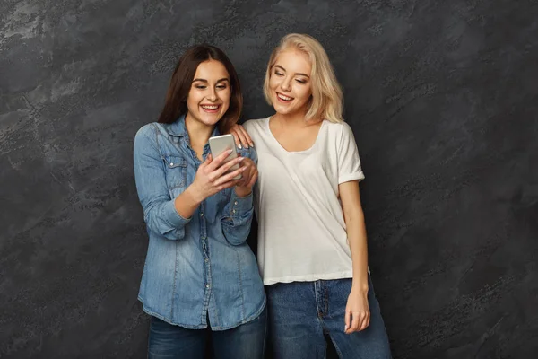 Happy women friends using smartphone at dark studio background — стоковое фото