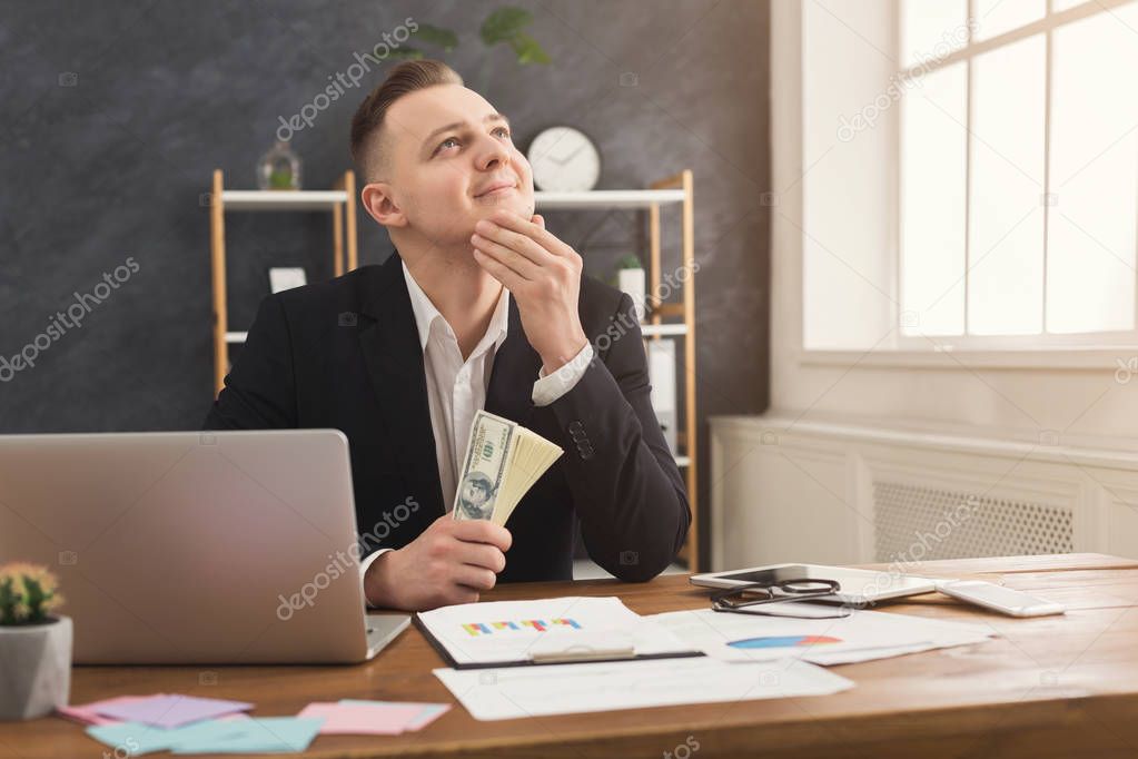 Financier man sitting in office and holding money in hand