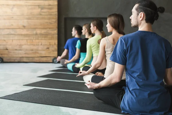 Mujeres jóvenes y hombres en clase de yoga, relajar la meditación pose — Foto de Stock