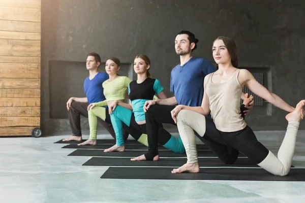 Mujeres y hombres jóvenes en clase de yoga, haciendo ejercicios de estiramiento — Foto de Stock