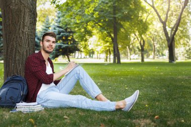 Açık havada çimenlerin üzerinde oturan genç yakışıklı adam