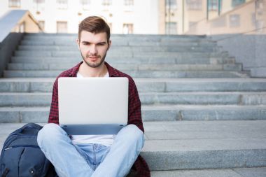 Dizüstü bilgisayar açık havada kullanarak merdivenlerde oturan öğrenci