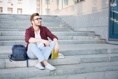 Açık havada defter ile merdivenlerde oturan genç adam