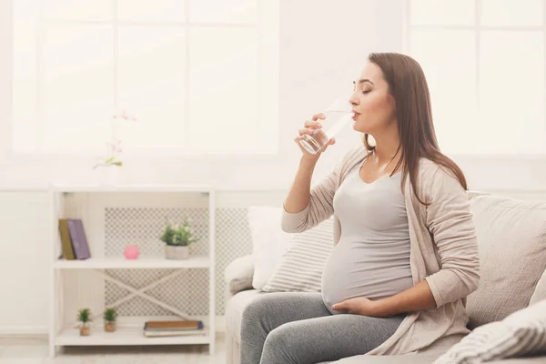 Mujer embarazada bebiendo agua sentada en el sofá — Foto de Stock