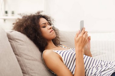 Kanepenin üzerinde cep telefonu kullanan genç kız üzgün
