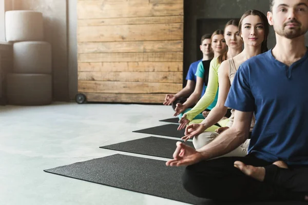 Jovens mulheres e homens na aula de ioga, relaxe a postura de meditação — Fotografia de Stock