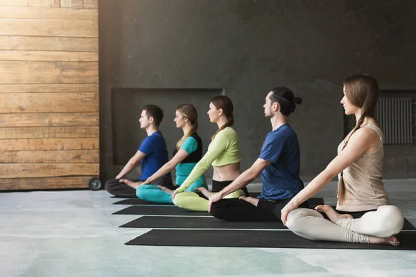 Mujeres jóvenes y hombres en clase de yoga, relajar la meditación pose — Foto de Stock