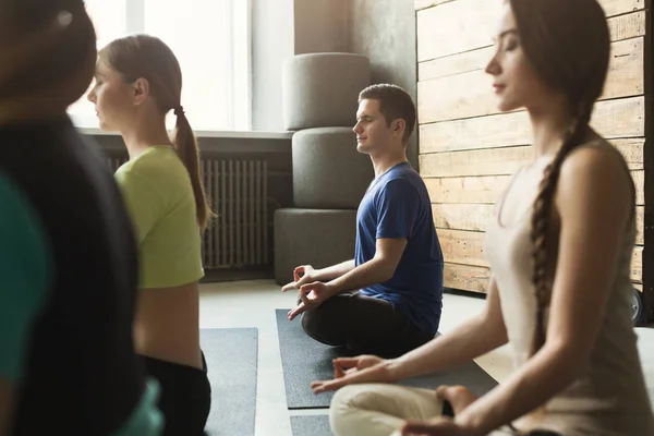 Молодые женщины и мужчина в классе йоги, расслабиться медитации позы — стоковое фото