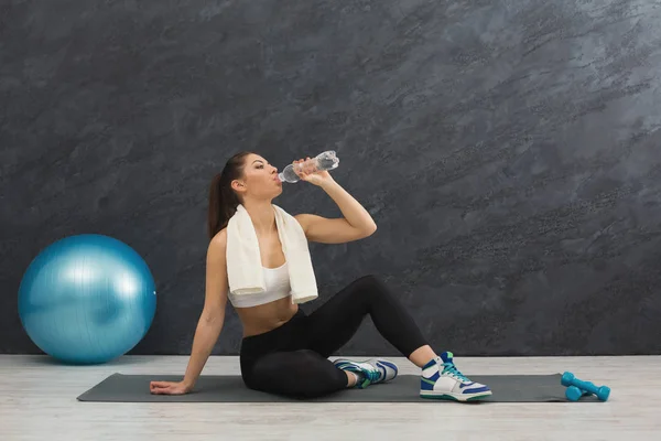 Фитнес-женщина питьевая вода в тренажерном зале на сером фоне — стоковое фото