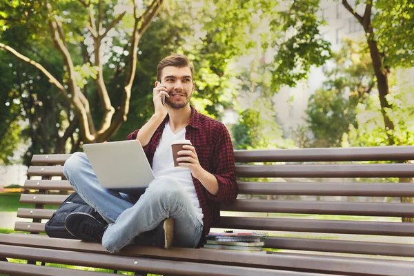 Homem com laptop, falando no smartphone ao ar livre — Fotografia de Stock