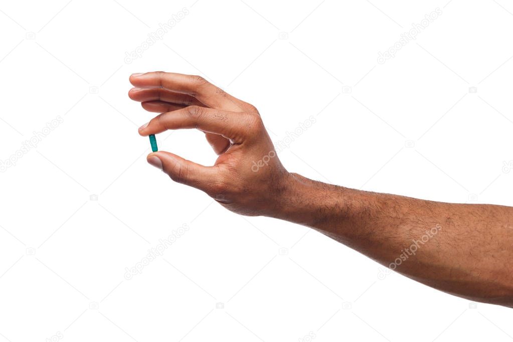 Black hand holding a pill isolated on white background