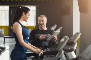 Spor hocası eliptik eğitmen kadına yardımcı olur.