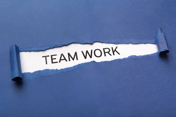 Texte Travail d'équipe sur fond blanc apparaissant derrière du papier bleu déchiré — Photo