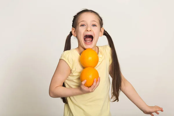 Glückliches kleines Mädchen hat Spaß mit Orangen auf weißem Hintergrund — Stockfoto